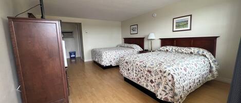A bedroom with two beds, a wooden dresser, a lamp, and a framed picture on the wall.