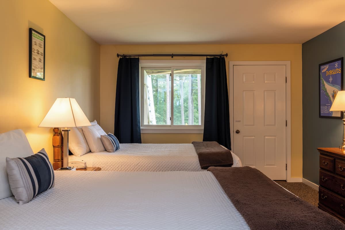 A hotel room with two beds, a window with curtains, a door, and a dresser.