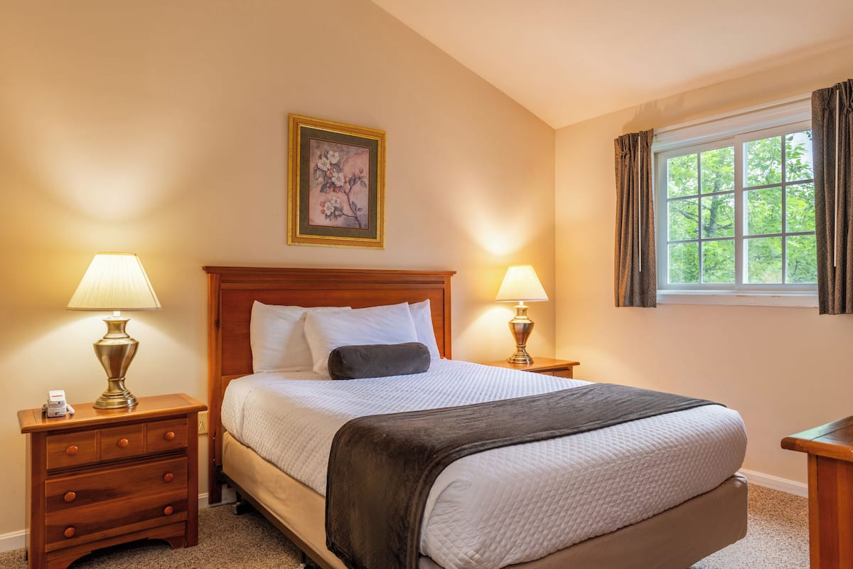 A hotel room with a large bed, two bedside tables with lamps, a painting on the wall, and a window with curtains.