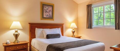 A hotel room with a large bed, two bedside tables with lamps, a painting on the wall, and a window with curtains.