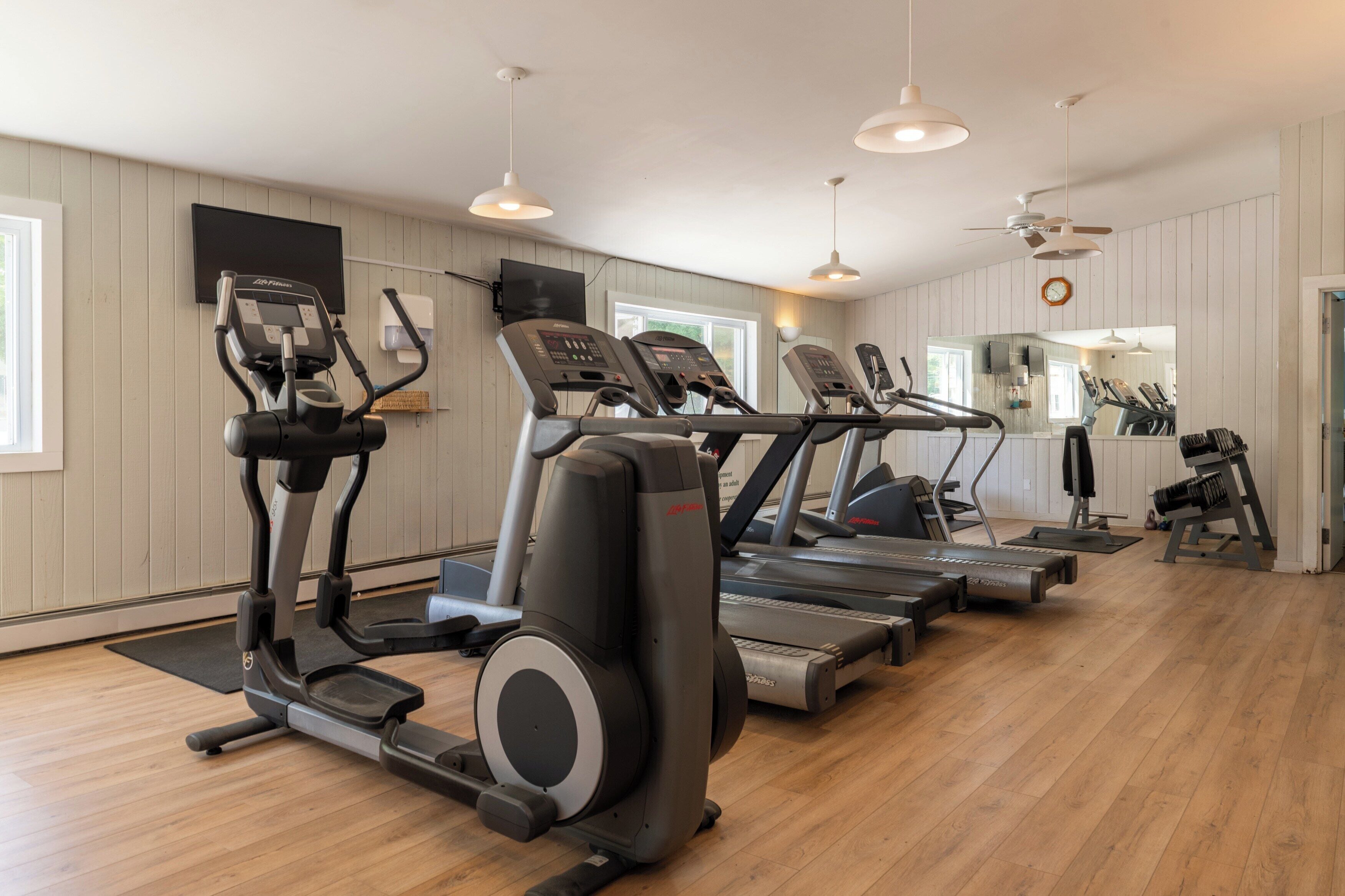 A gym with treadmills, ellipticals, and a mirrored wall.