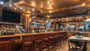 Un espace bar avec des meubles en bois, un comptoir où sont exposées des bouteilles, et une enseigne indiquant « The Tavern ».