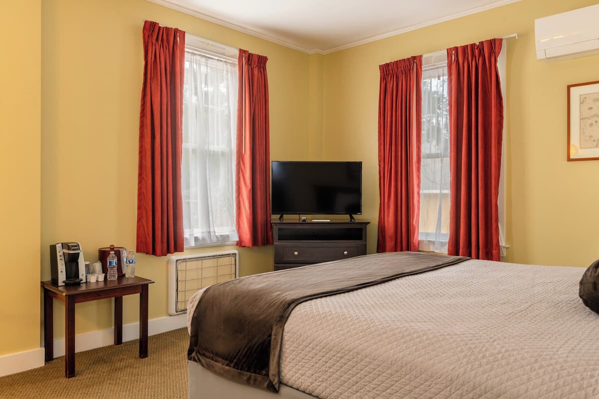 A hotel room with a bed, a television, a small table with a coffee maker, and a radiator.