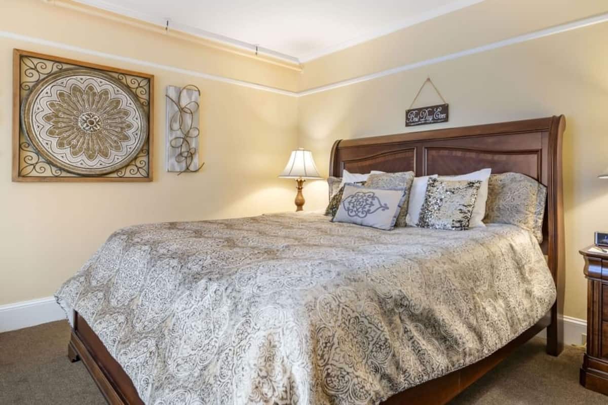 A bedroom with a large bed, two bedside tables with lamps, a clock, and decorative wall art.