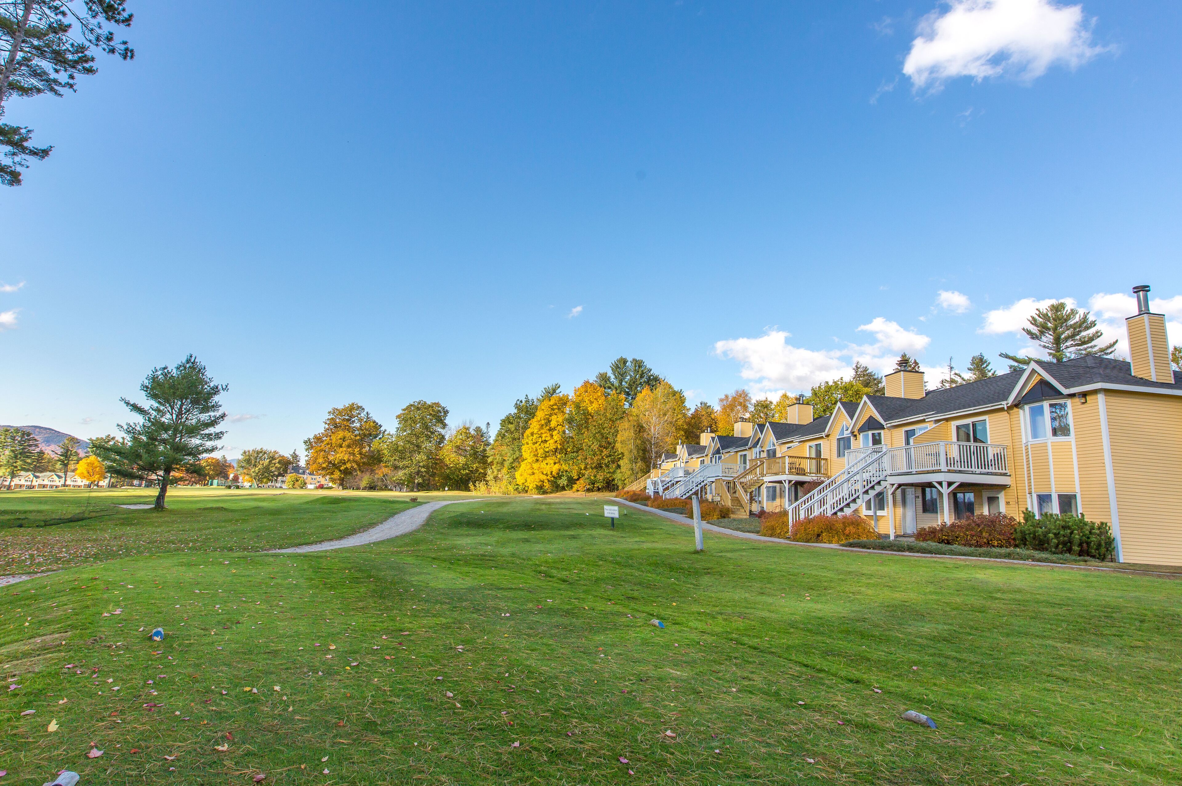 Un área residencial con un campo de golf, un sendero para caminar y una fila de casas amarillas con balcones y una escalera que conduce a la entrada.