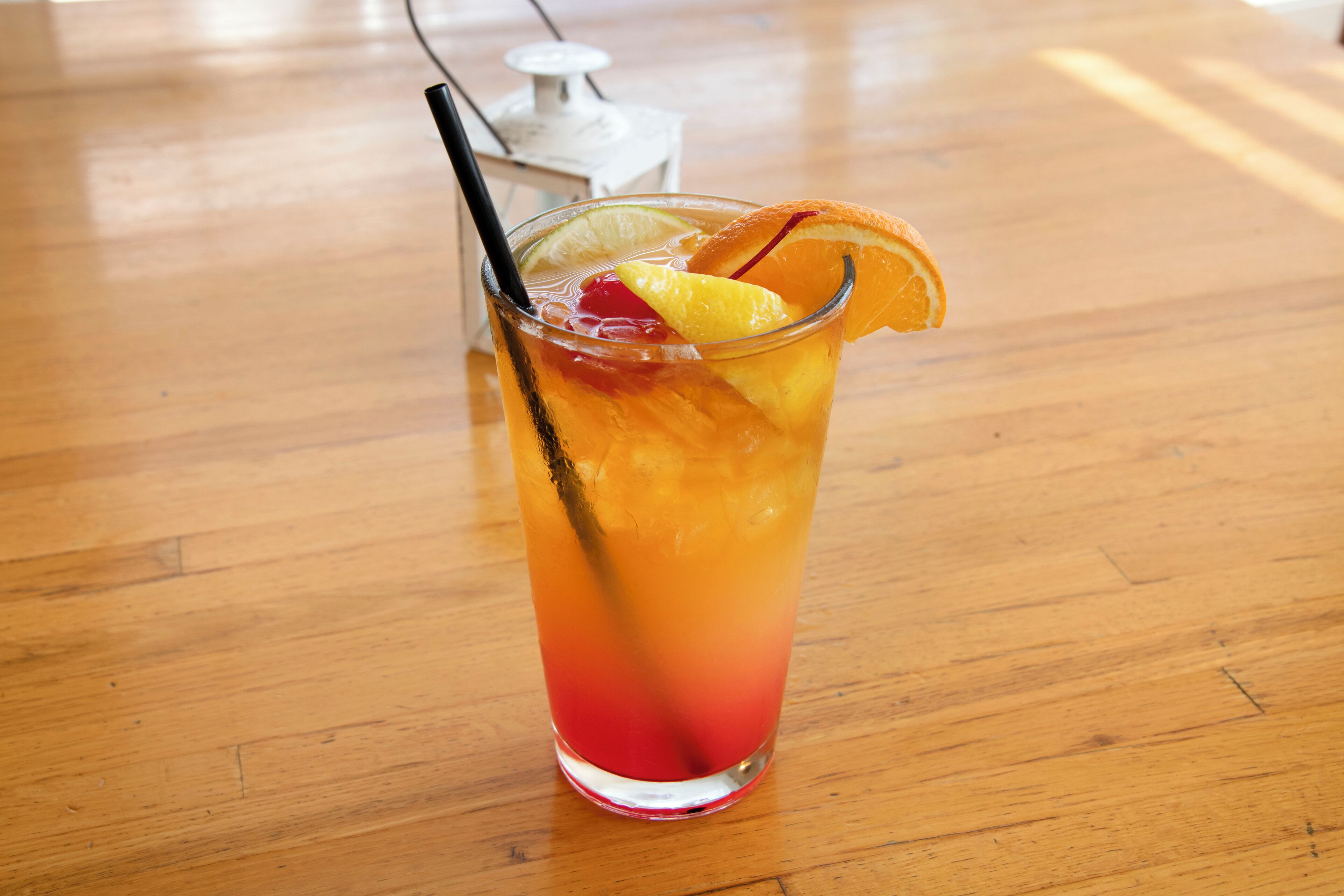 A tall glass with a gradient color, containing a beverage and garnished with fruit.