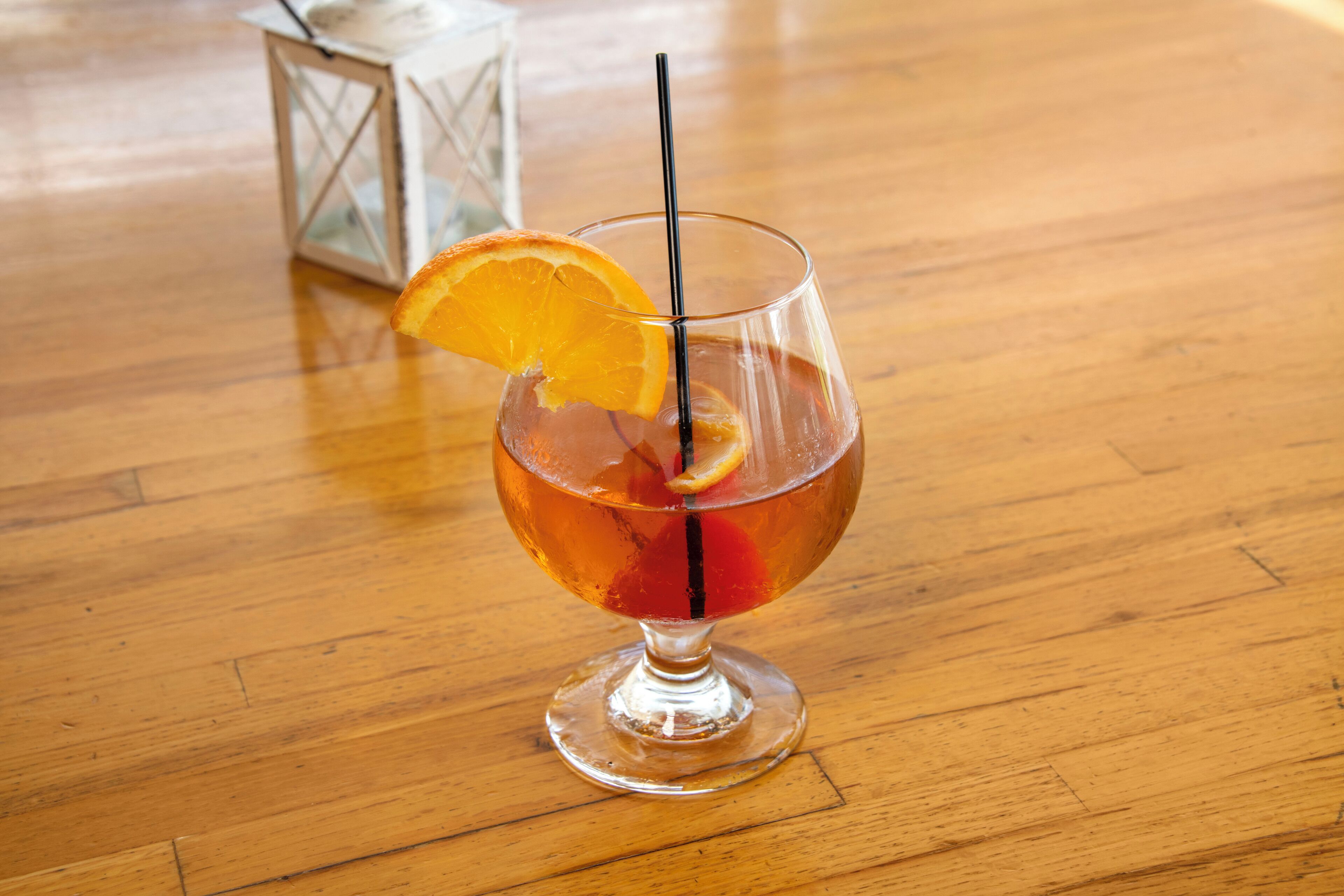 A cocktail glass with an orange slice garnish on a wooden table.