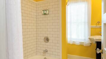 A bathroom with a white bathtub, a shower area with white tiles, and a yellow wall.