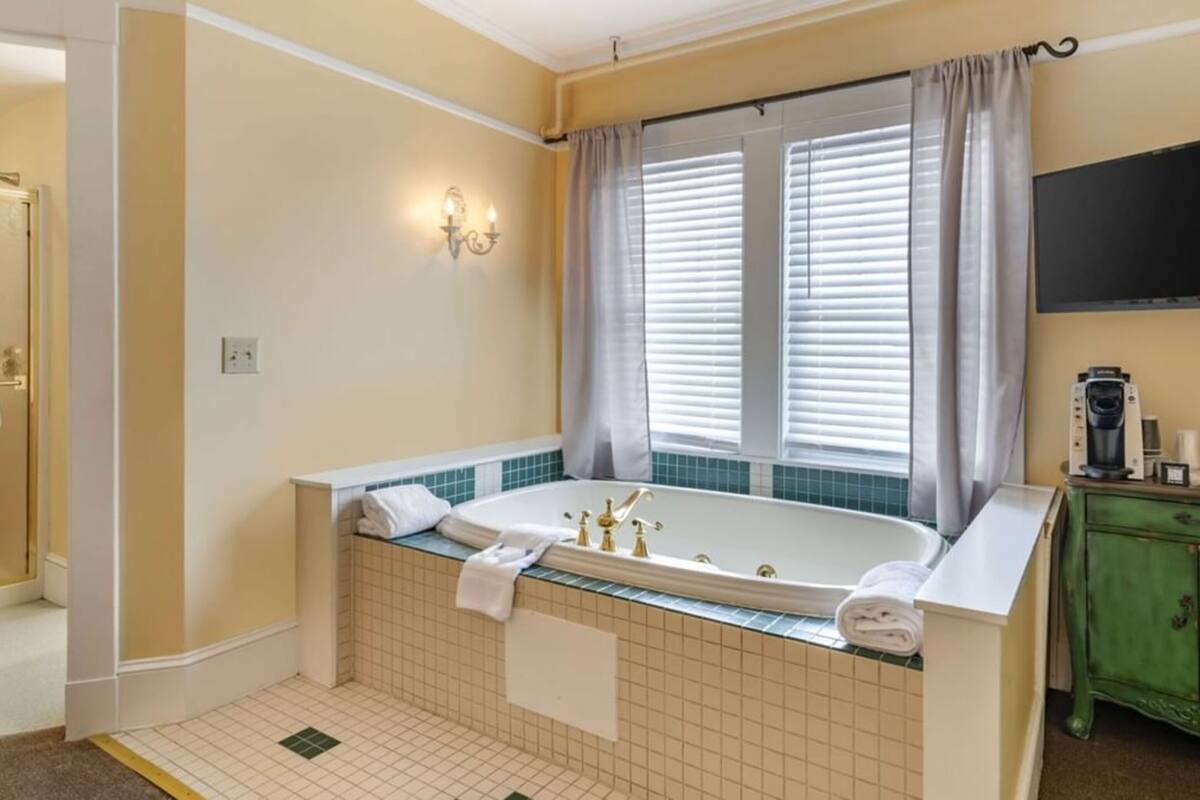A bathroom with a bathtub, a shower, a vanity with a mirror, and a window with blinds.