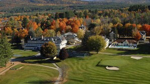 Un parcours de golf doté d’un club-house, entouré d’arbres aux couleurs automnales et avec une chaîne de montagnes en toile de fond.