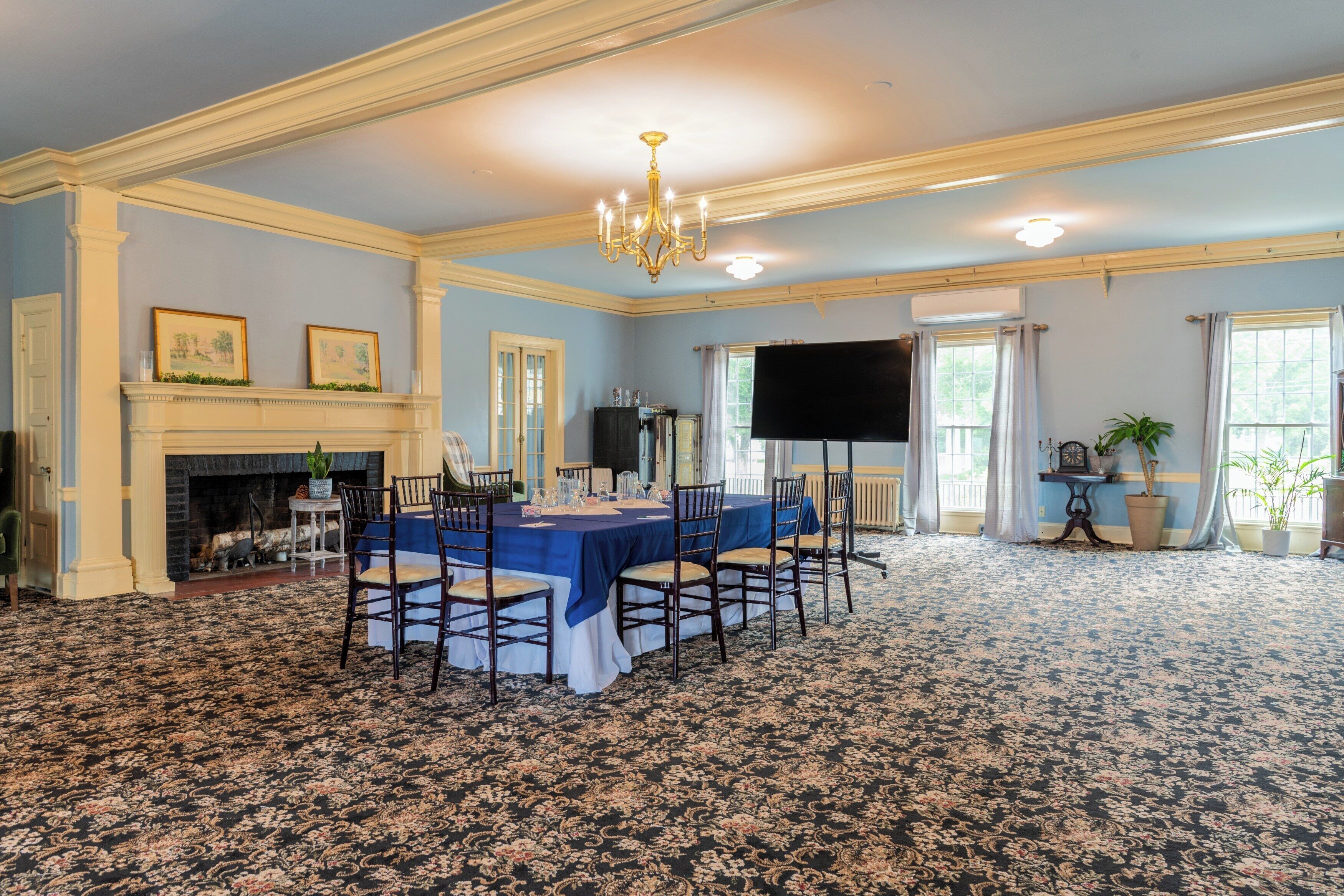 A formal dining room with a large table set for six, a fireplace, and a television screen.