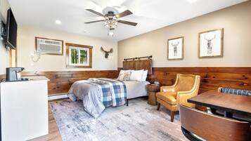 A bedroom with a bed, a desk, a chair, a table, a ceiling fan, and wall-mounted artwork.