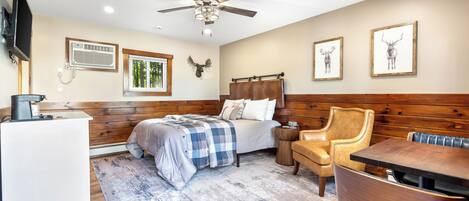 Un dormitorio con cama, escritorio, silla, mesa, ventilador de techo y obra de arte en la pared.