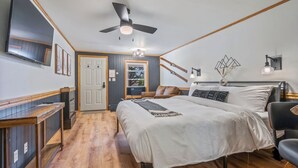 A bedroom with a large bed, a ceiling fan, a TV, and a desk. - The Inn at the Rostay (Bethel)
