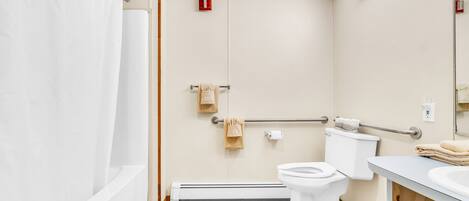Een badkamer met bad, toilet en wastafel. Er is een handgreep voor toegankelijkheid, een handdoekrek en een rookmelder.