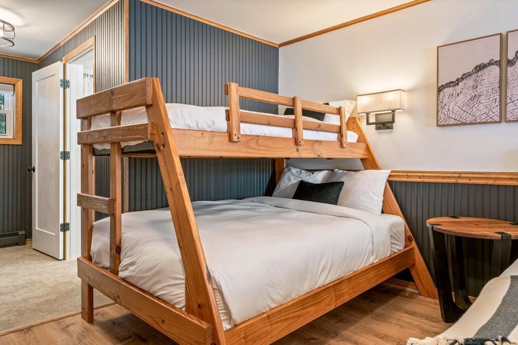 Un lit superposé avec une structure en bois et une literie blanche, dans une pièce dont un mur est bleu et qui contient une petite table ronde.