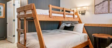 Un lit superposé avec une structure en bois et une literie blanche, dans une pièce dont un mur est bleu et qui contient une petite table ronde.