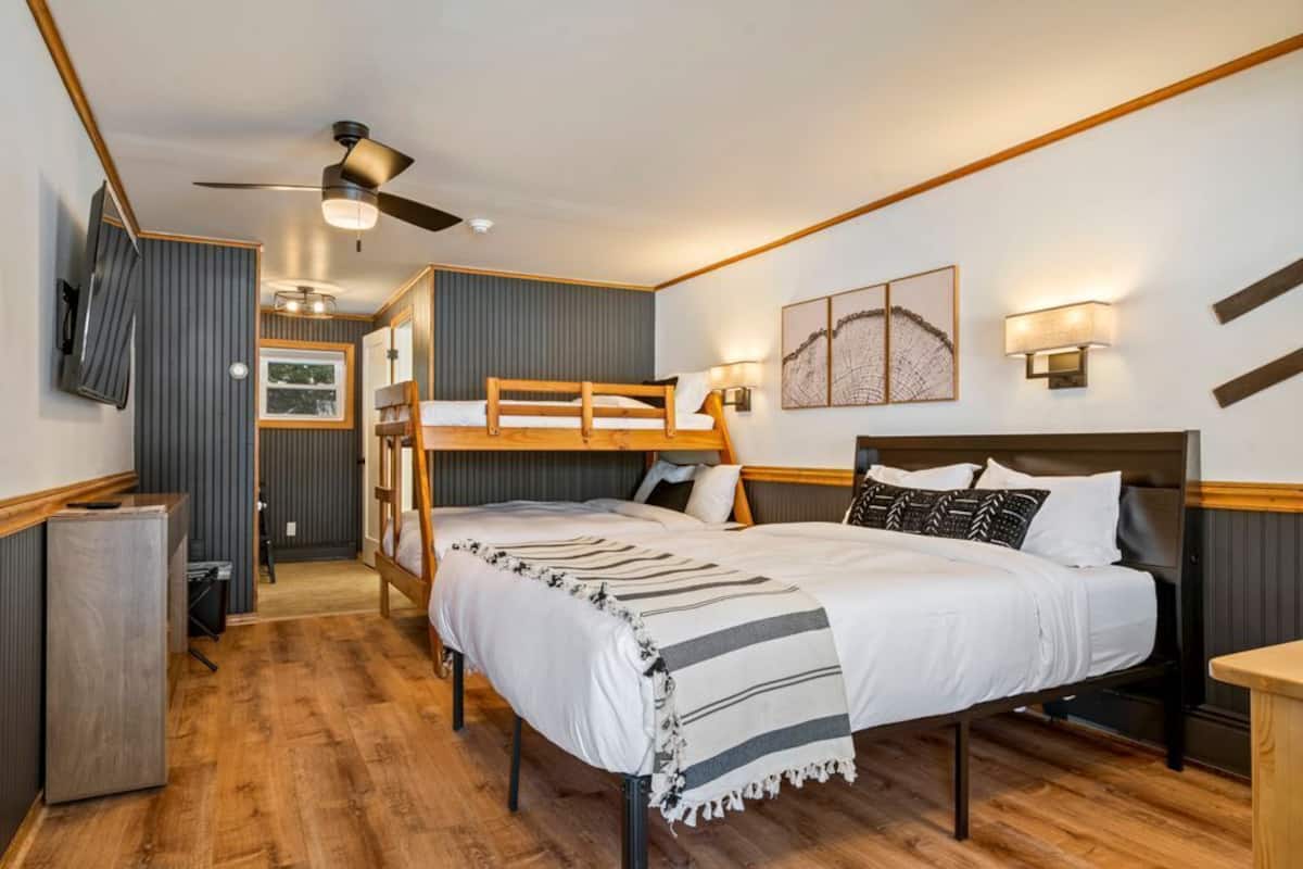 Une petite pièce comprenant un lit superposé, un bureau, un réfrigérateur et un ventilateur de plafond.