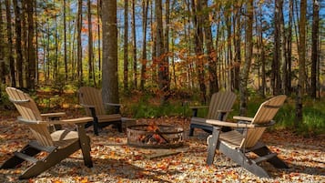 Een boslandschap met een vuurkuil en Adirondack-stoelen eromheen.