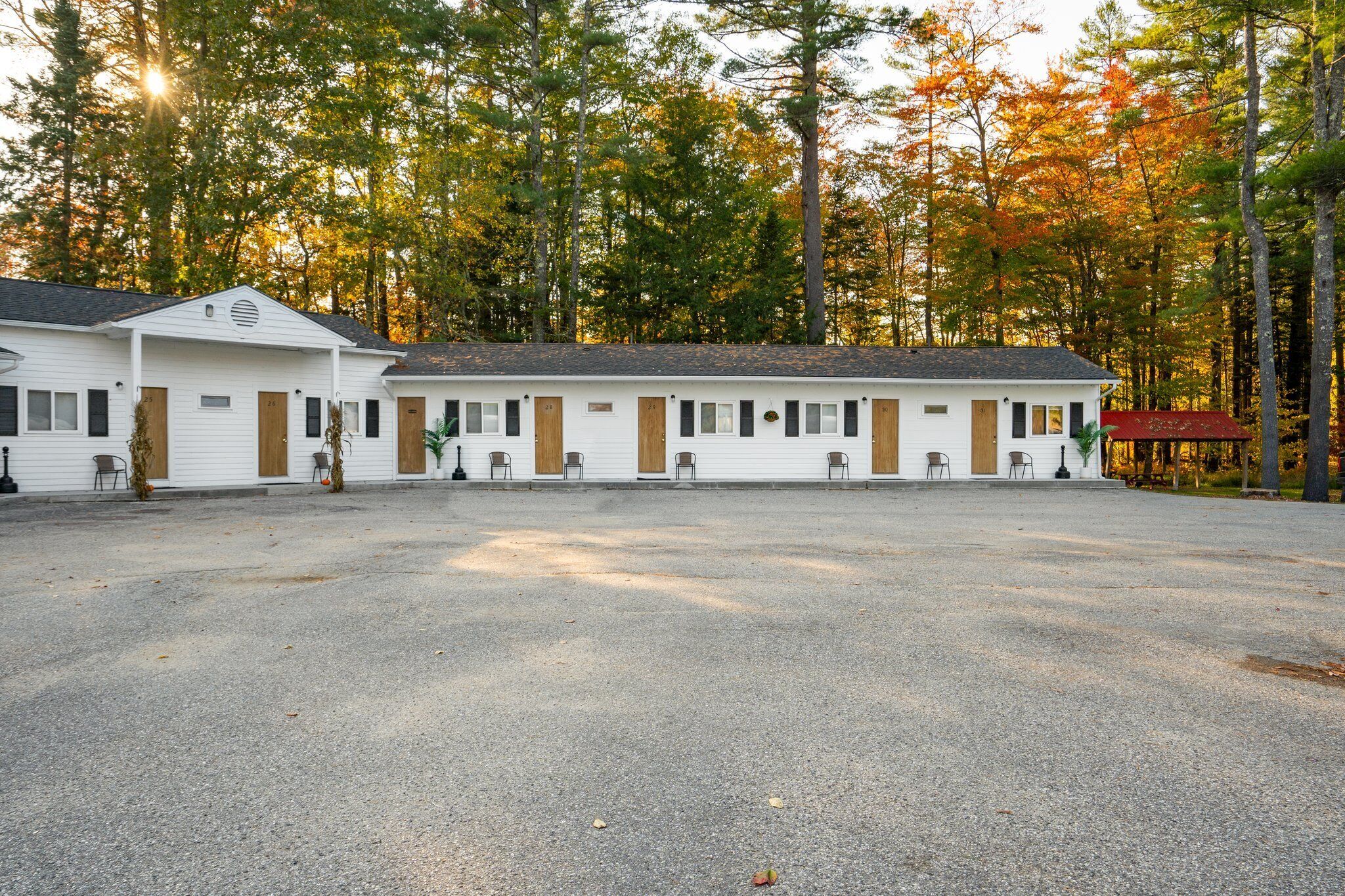 A motel with multiple rooms, each with a door and windows, set against a backdrop of autumn trees.