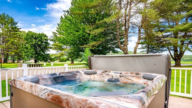A hot tub on a wooden deck with a view of trees and a grassy area. - The Inn at the Rostay (Bethel)