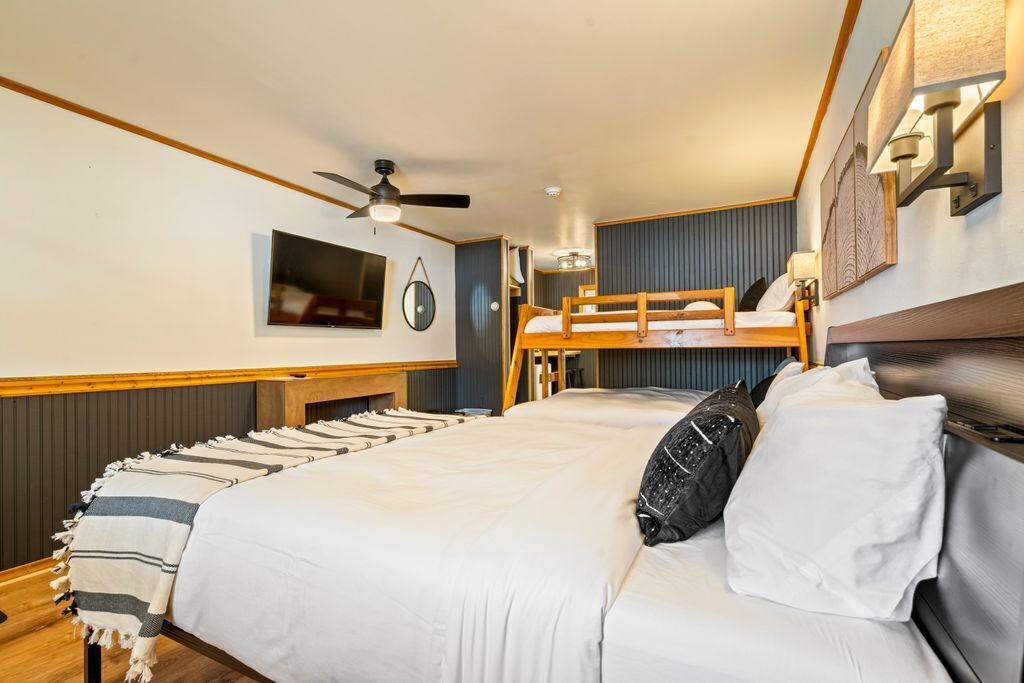 A bedroom with a bunk bed, a flat-screen TV, a ceiling fan, and a bed with a striped blanket.