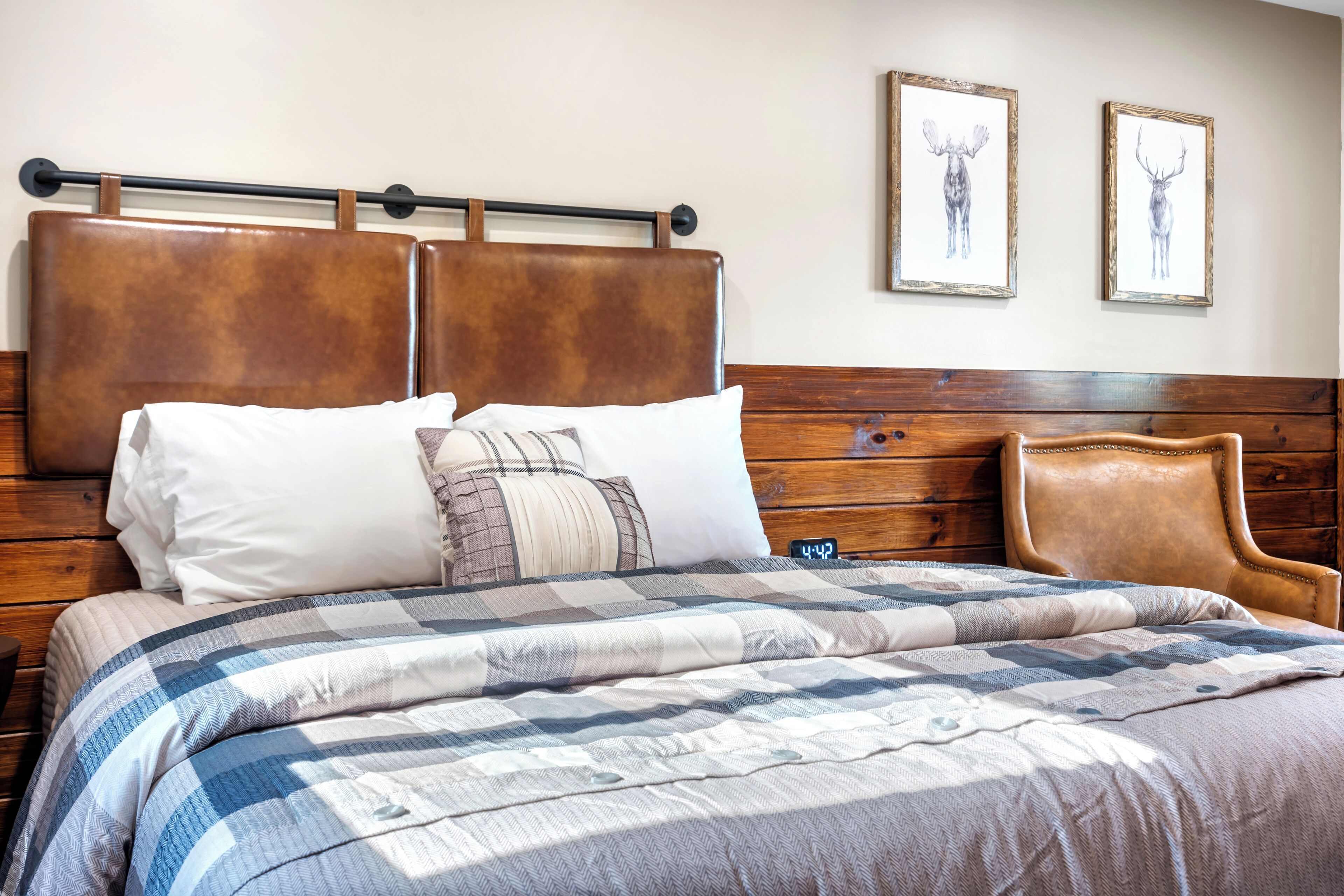 A neatly made bed with a checkered bedspread, a wooden headboard, and two framed animal prints on the wall.
