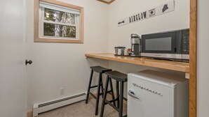 A compact kitchen with a microwave, coffee maker, and a refrigerator. There is a window with a view of trees and a sign above the counter that reads "AIRGLOW." - The Inn at the Rostay (Bethel)