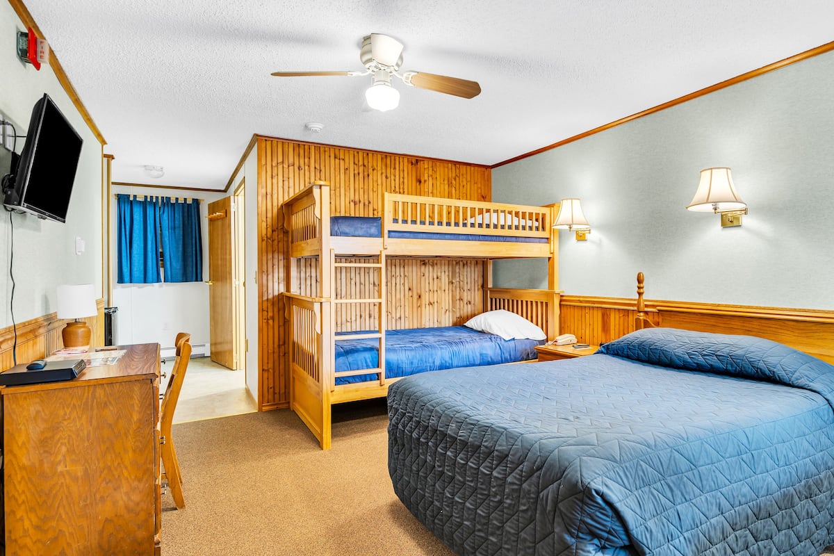 Une chambre avec un lit superposé, un bureau, une chaise, une télévision et un ventilateur de plafond.