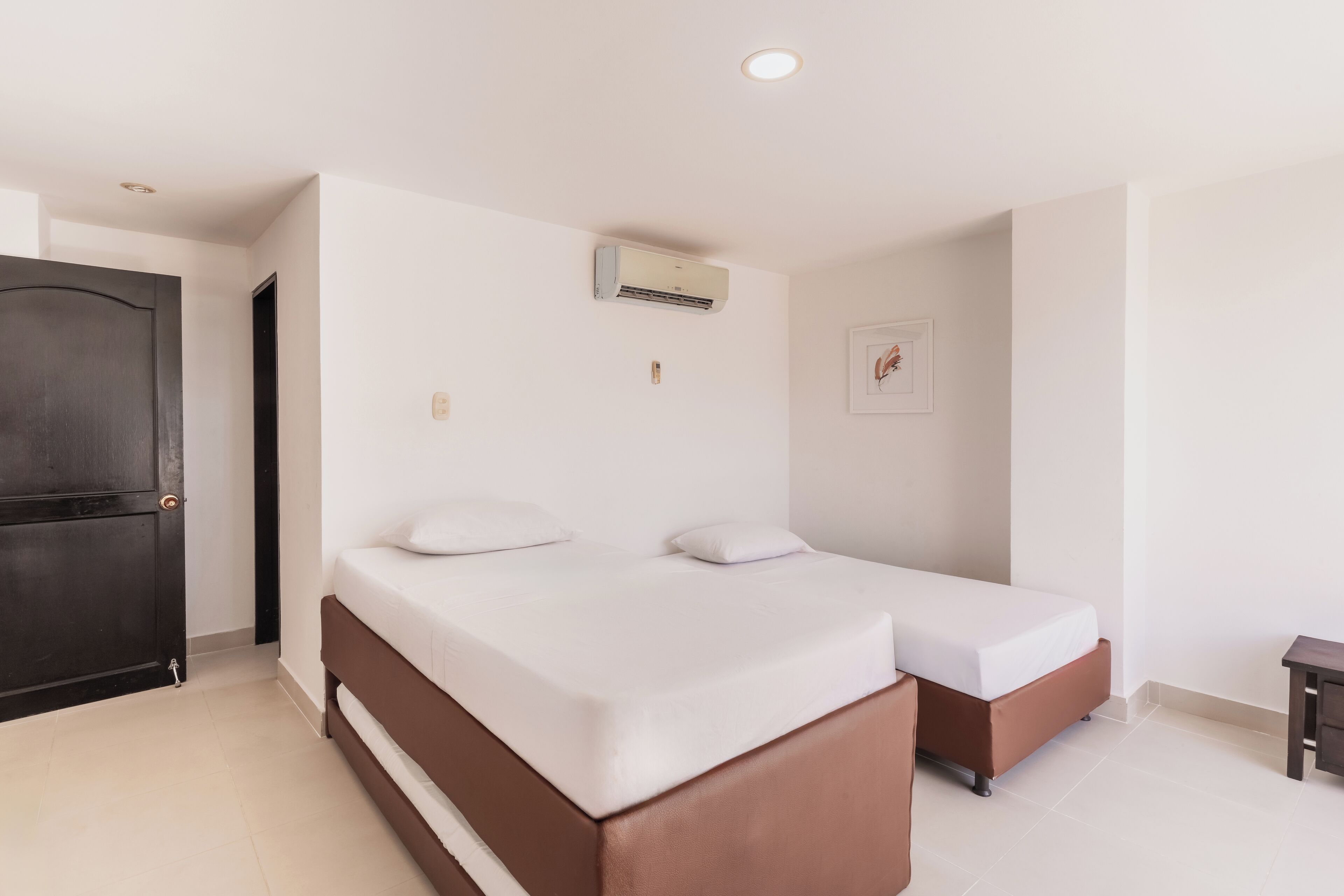 Een kamer met twee bedden, een donkere deur, een airconditioning en een klein tafeltje.