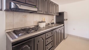 Une cuisine avec des meubles de couleur sombre, une cuisinière à gaz, un évier et un réfrigérateur.