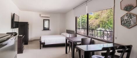 A hotel room with a bed, a dining table with chairs, a TV, and a window with a view of trees.