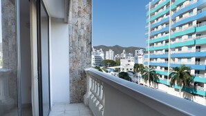 Un balcon offrant une vue sur le paysage urbain, avec notamment un grand immeuble bleu et des palmiers.