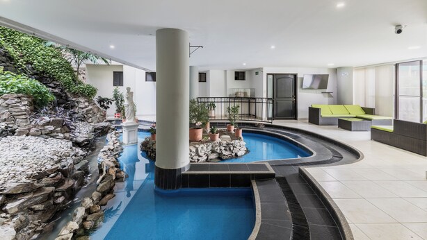 Un espace piscine agrémenté d’une cascade en pierre, de plantes en pot et de mobilier d’extérieur.
