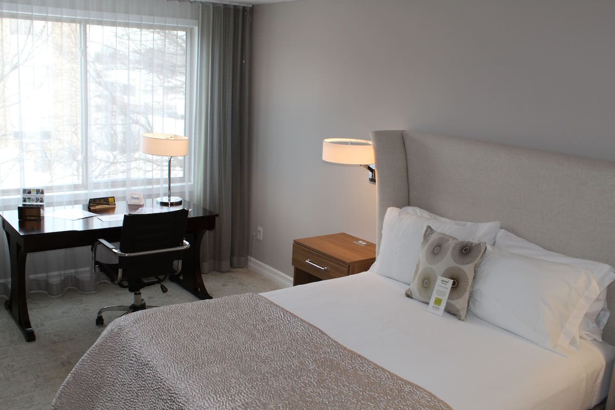 Ein Hotelzimmer mit Bett, Schreibtisch, Stuhl, Lampe und Nachttisch.