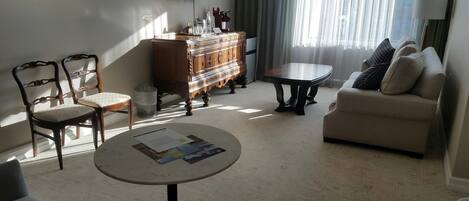 A living room with a sofa, two armchairs, a coffee table, a TV, a cabinet, and a window with curtains.