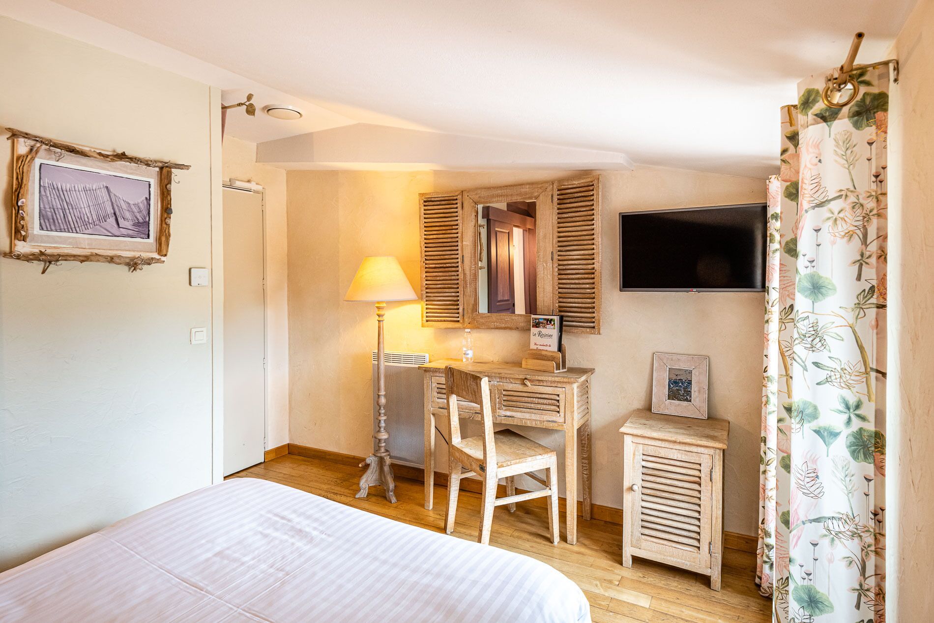 A bedroom with a bed, a desk, a chair, a small cabinet, a mirror, and a television.