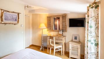 A bedroom with a bed, a desk, a chair, a small cabinet, a mirror, and a television.