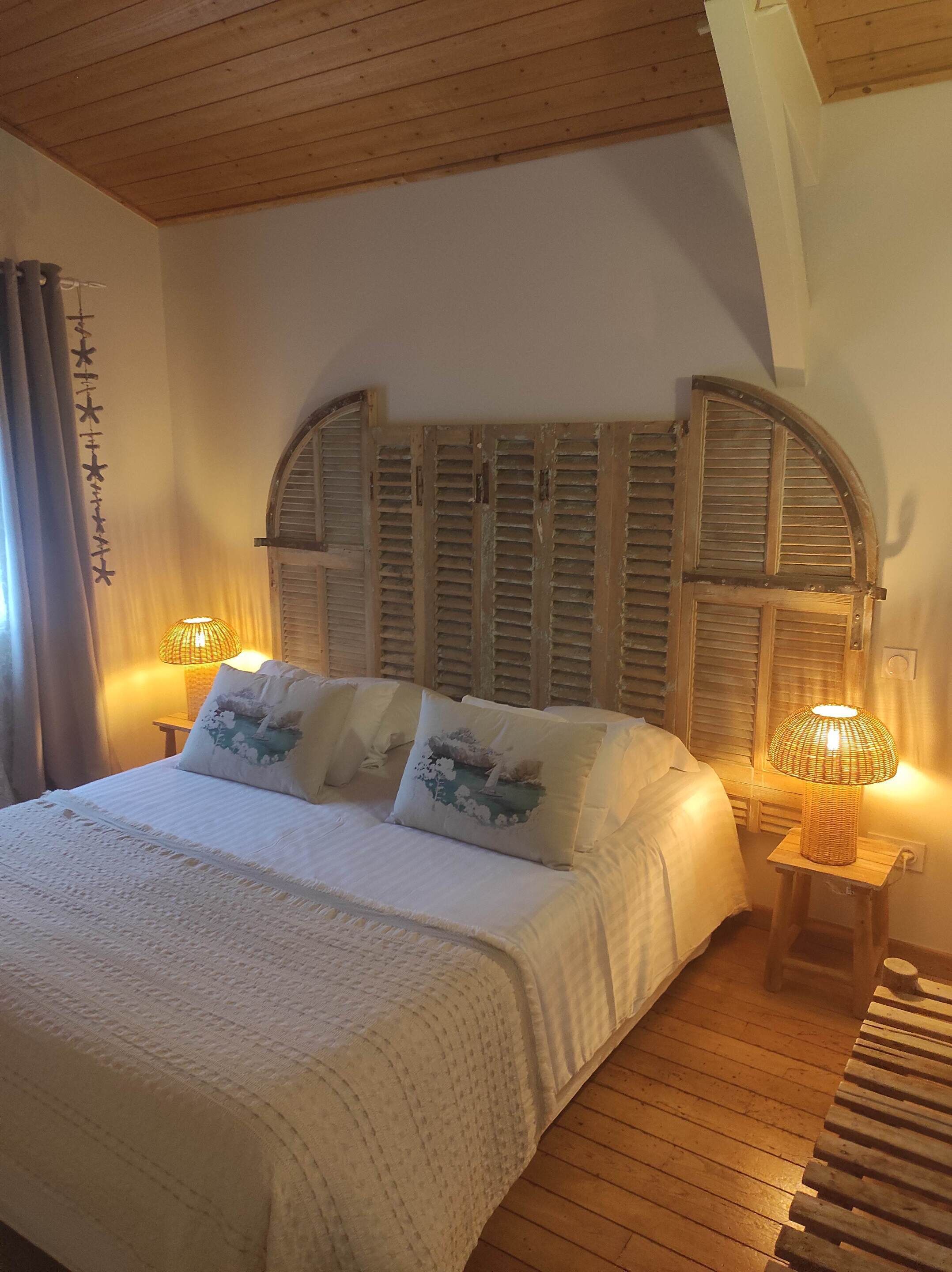 Un dormitorio con techo de madera, una cama con ropa de cama blanca, dos lámparas de noche y un panel decorativo en la pared.