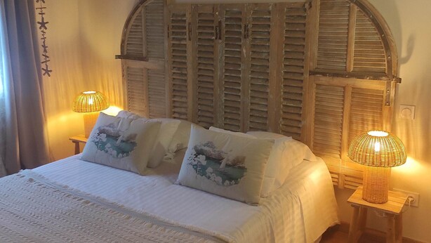 A bedroom with a wooden ceiling, a bed with white bedding, two bedside lamps, and a decorative wall panel. - Hôtel Le Résinier (Le Barp)