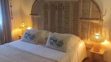Un dormitorio con techo de madera, una cama con ropa de cama blanca, dos lámparas de noche y un panel decorativo en la pared.