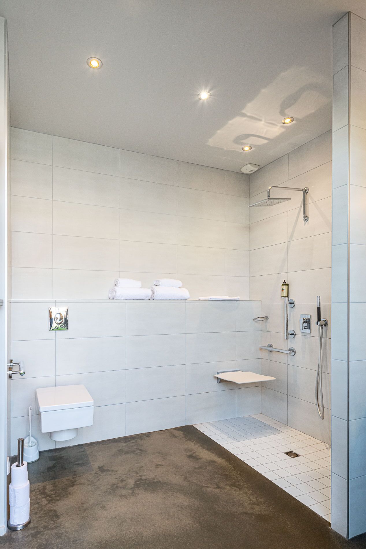 A modern bathroom with white tiles, a shower, a toilet, and a sink.