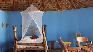 Una habitación con una cama bajo un techo de paja, muebles de madera y una pared azul.