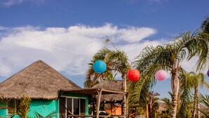 Zona de piscina con un edificio de techo de paja, palmeras y cielo despejado.
