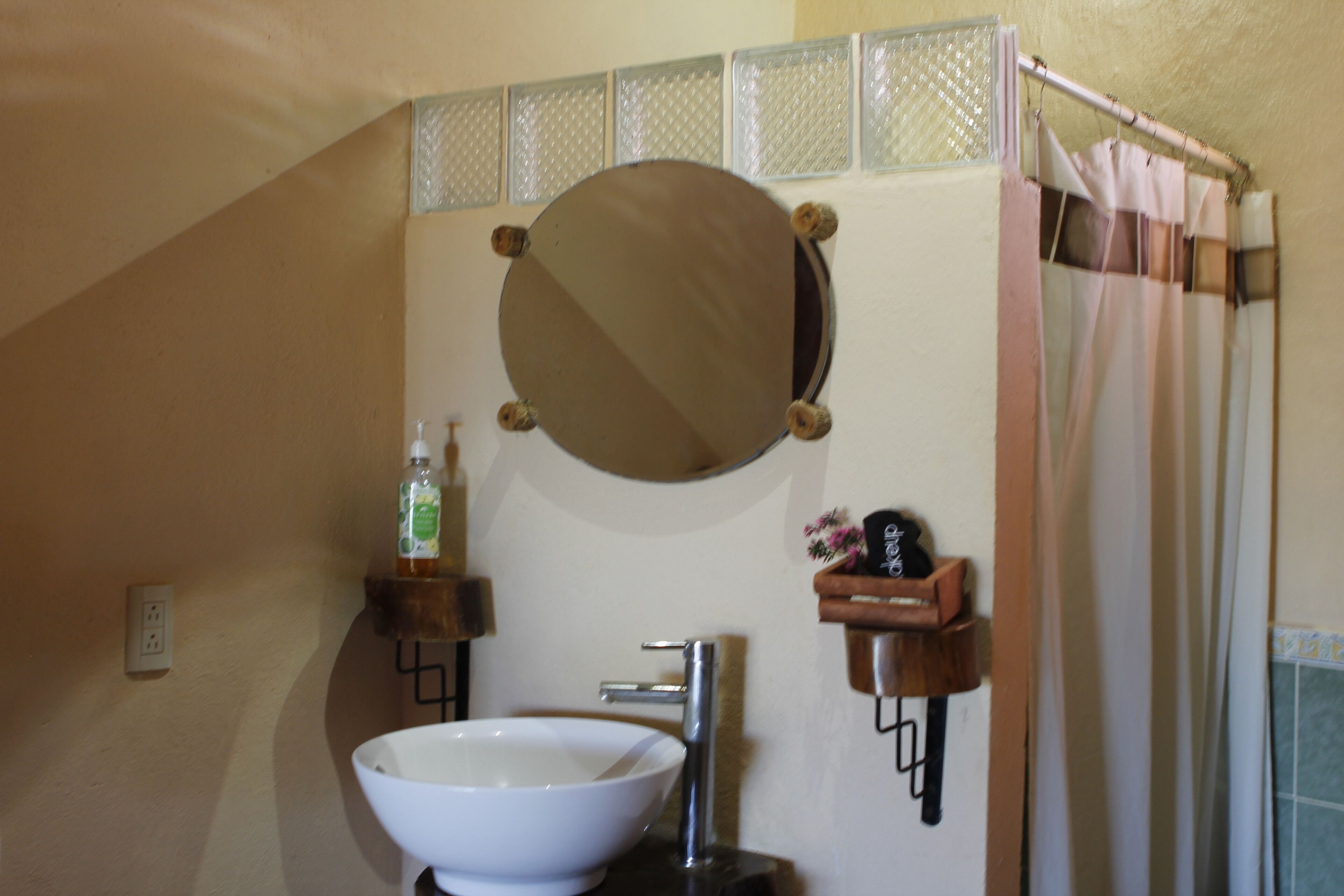 Une salle de bain avec un lavabo blanc, un miroir rond et un rideau de douche.