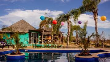 Relax by the tranquil pool surrounded by palm trees and a thatched-roof structure.
