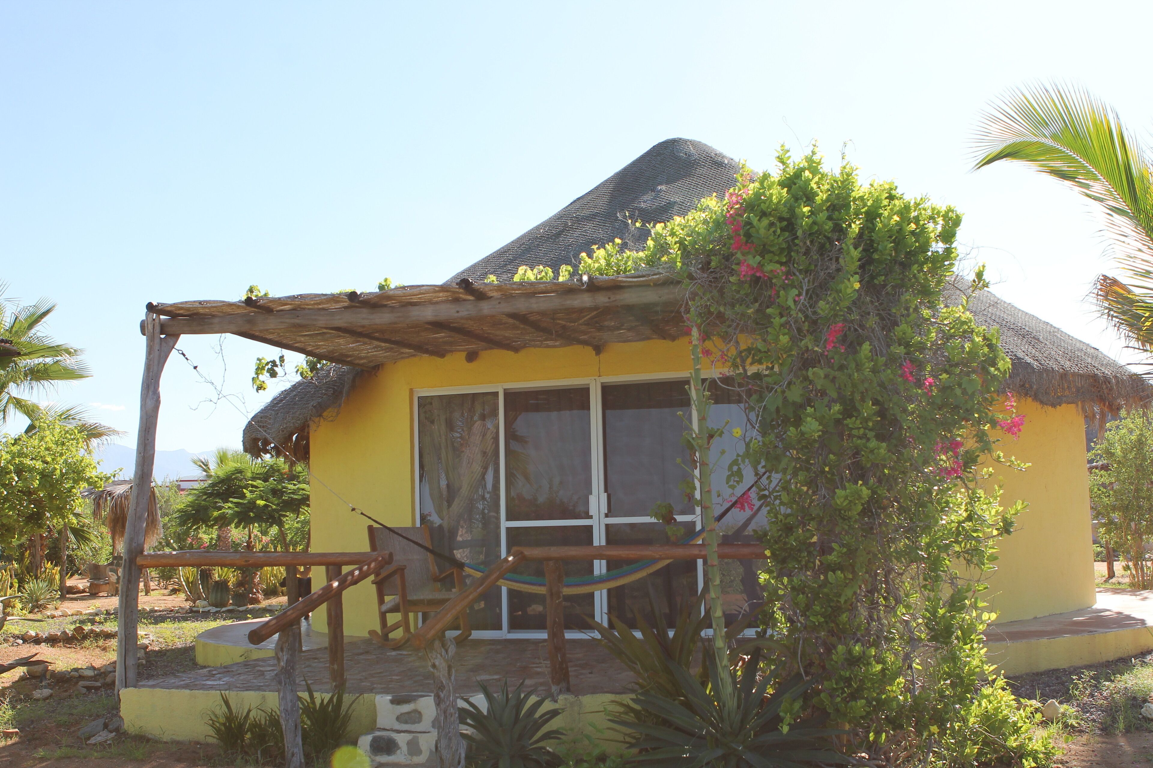 A yellow building with a thatched roof, a wooden porch, and a sliding glass door.