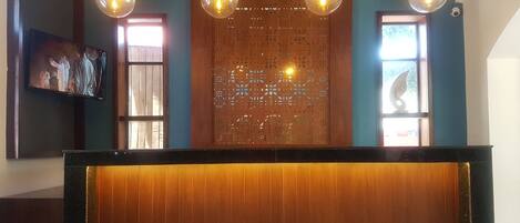 A reception area with a wooden reception desk, a decorative wall with cut-out patterns, and three hanging pendant lights.