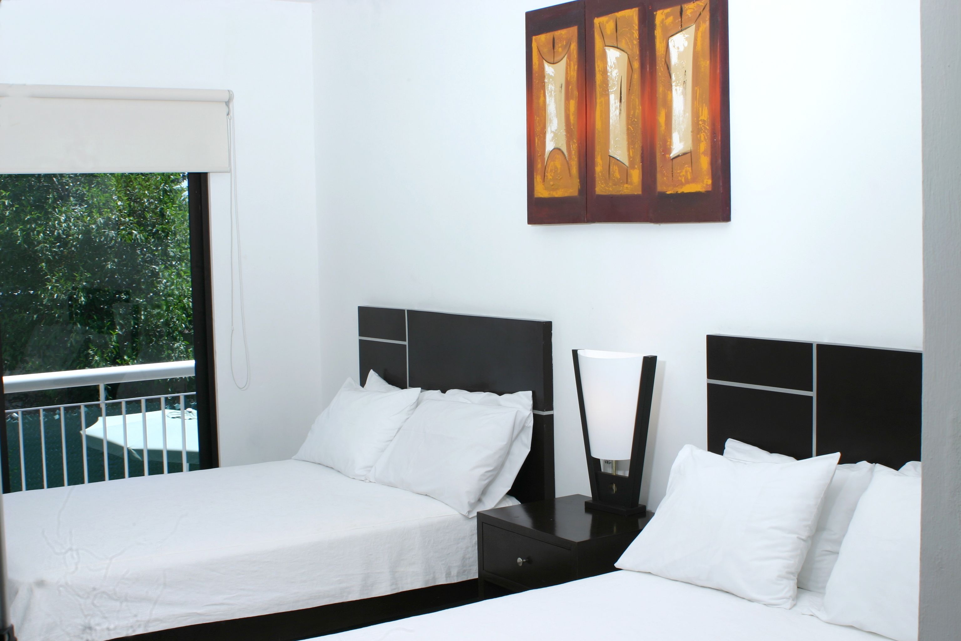 A hotel room with two beds, a nightstand with a lamp, and a window with a view of trees.