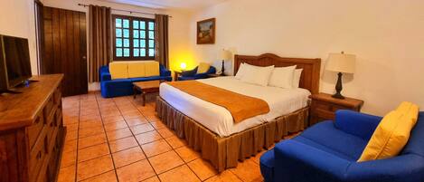 Une chambre d’hôtel avec un lit, un canapé bleu, une commode en bois, une télévision et une fenêtre avec des rideaux.